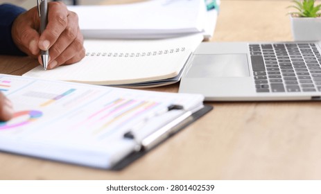 Business professional taking notes while analyzing financial reports and performance charts at office desk, representing data analysis, strategic planning, productivity, reporting, and business management.