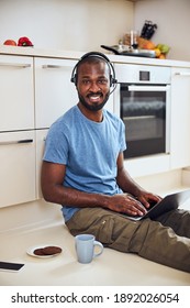 Business professional wearing headphones while working on a laptop with tea and biscuits beside him - Shutterstock ID 1892026054