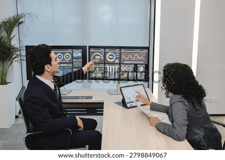 Business professionals analyzing data and discussing financial reports with digital dashboards and graphs in a modern office setting, focusing on strategy and performance.
