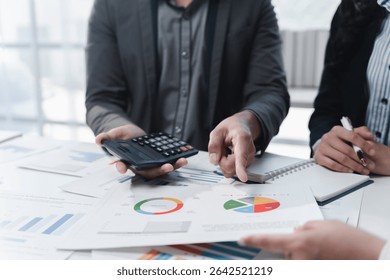 Business professionals analyzing financial data, using calculators, and pointing at pie charts on desks during corporate meetings, highlighting teamwork and collaboration in the office environment