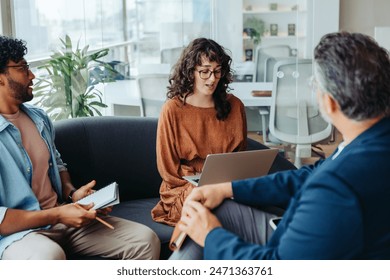 Business professionals collaborating in an office, discussing a project. They sit on a couch, working together on a laptop. Colleagues contributing to creative brainstorming, demonstrating teamwork. - Powered by Shutterstock