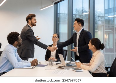 Business professionals engaged in meeting room. Two colleagues in formal attire shaking hands over conference table, symbolizing teamwork, collaboration, success. Diverse team involved. - Powered by Shutterstock