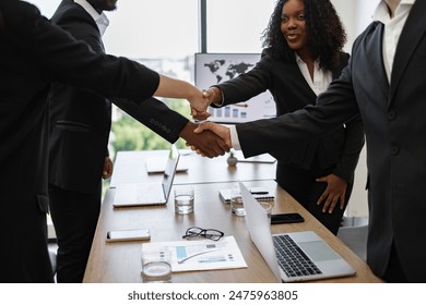 Business professionals in formal attire shaking hands across a conference table, symbolizing successful agreement or deal in a modern office setting. - Powered by Shutterstock