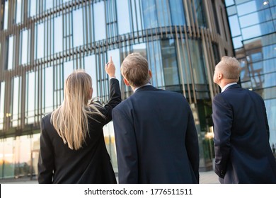 Business Professionals In Suits Looking At Office Building Facade, Pointing Up, Discussing Real Property. Back View, Low Angle. Commercial Real Estate Concept