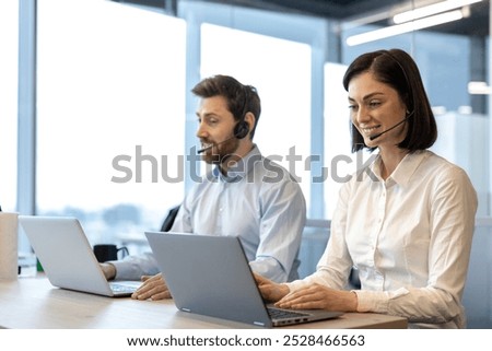 Business professionals using headsets while working on laptops in office setting. Call center employees discussing client communication, focused on providing excellent customer service.