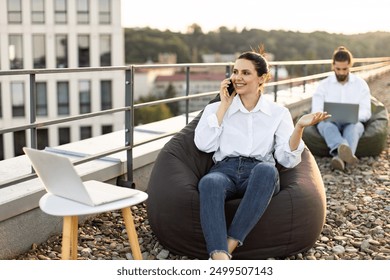 Business professionals working remotely on outdoor rooftop lounge, using laptops and smartphones. Relaxed work, casual attire, and modern workspace setting. Ideal for collaborative work scenes. - Powered by Shutterstock