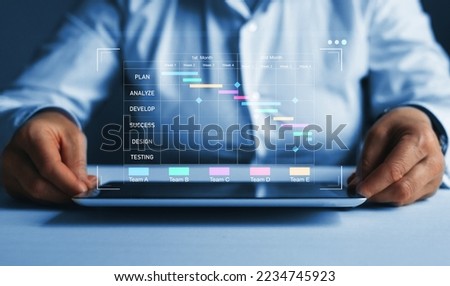  Business Project Management System. Project manager working on laptop and updating tasks and milestones progress planning with Gantt chart scheduling interface for company on virtual screen.