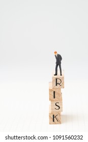 Business risk assessment or management concept with miniature figure businessman standing on top of unstable wooden blocks tower with alphabets combine word RISK on grid notebook and white copy space. - Shutterstock ID 1091560232