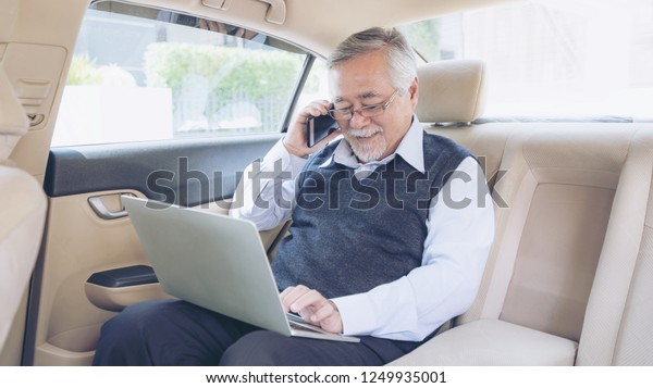 Business senior rich man Stock trader\
player in suit working with laptop computer and using a smart phone\
in his car , concept for senior business success\

