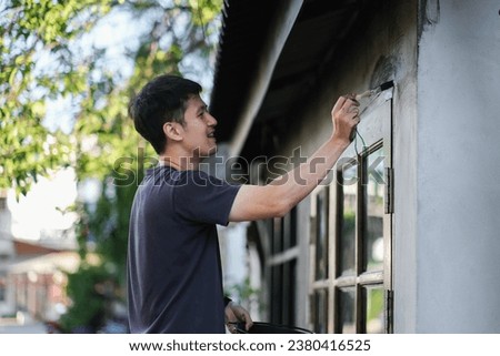 Business shop owner renovating and decorating his store painting on the wall of his front store using a paintbrush. Happy smiling Asian male handsome local startup restaurant.
