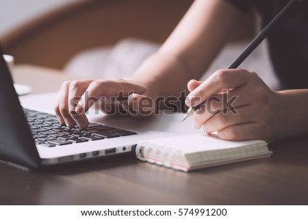 Business situation, female using laptop to get information and memo into paper