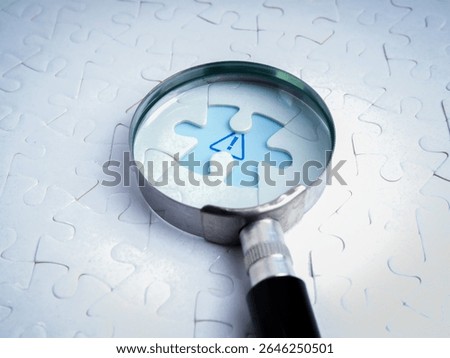 Business solutions, problems found, problem solving concept. Close-up blue caution sign, graphic on space of last missing piece, focus in magnifying glass lens, on white jigsaw puzzle background.