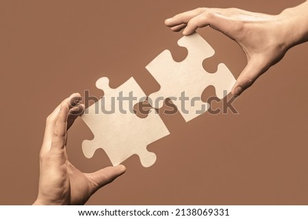 Business solutions, success and strategy concept. Two hands trying to connect couple puzzle piece on gray background. Teamwork concept. Closeup hand of connecting jigsaw puzzle.