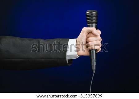 Business speech and topic: a man in a black suit holding a black microphone on a dark blue background in studio isolated