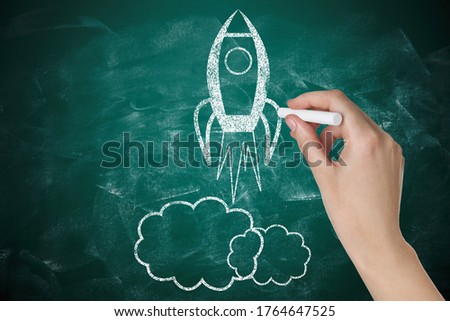 Business startup concept. Woman drawing rocket on chalkboard, closeup