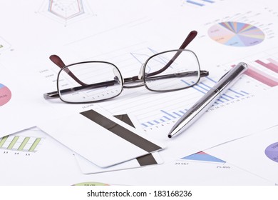 Business still-life of pen, charts, tables, eyeglasses, credit Cards