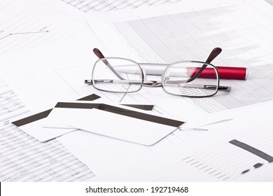 Business still-life of pen, charts, tables, eyeglasses, credit Cards
