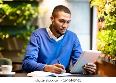 Business Strategy Analysis. Black Salesman Working In Cafeteria, Holding Tablet And Writing Work Process In Notepad