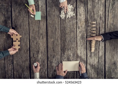 Business Strategy And Brainstorming Concept With A Team Of Six Businessmen Holding Puzzle Pieces, Writing Down Ideas On Paper And Stopping Domino Effect, Top View.