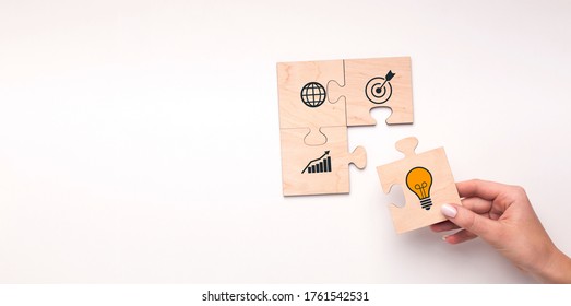Business Strategy Concept. Woman putting piece of puzzle with illustrated lightbulb as symbol of idea. Target, success and globe icons drawn on jigsaw