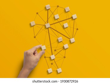 Business strategy, business management or business success concept. Hand is arranging wooden blocks in low polygon light bulb shape network on yellow background.