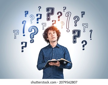 Business Student Man With Notebook, Looking For Answers. Background Of Doodle Question Marks Drawn On Blue Wall. Concept Of Career Development And Education