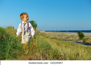 business style baby boy walking through the field near the sea