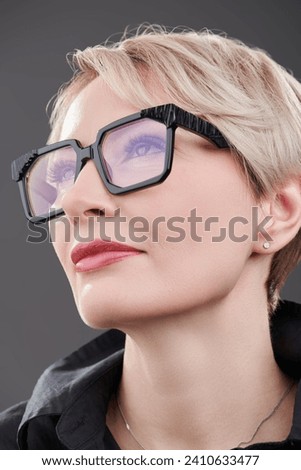 Business style and fashion for glasses. Close-up portrait of an elegant mature woman with a short haircut posing in stylish glasses. Gray studio background.