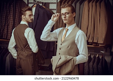 Business Style. Men's Fashion. Two Handsome Respectable Men In Elegant Classic Suits And Glasses Stand Together In A Premium Men's Clothing Store.
