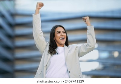 Business Success, Career Achievement. Joyful Arabic Business Lady Shaking Arms In Yes Gesture, Standing Outside In Urban Area, Near Modern Office Center Building. Triumph Celebration Concept - Powered by Shutterstock