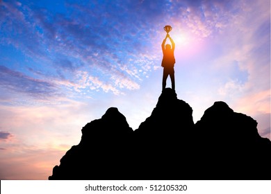 Business success concept.Silhouette of victory businessman hold winner trophy on top,peak of the mountain with sunset sky as background - Shutterstock ID 512105320
