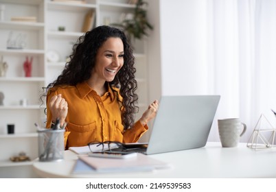 Business Success. Happy Brunette Lady Using Laptop And Gesturing Yes Shaking Fists Celebrating Big Luck Working Online Sitting In Modern Office Indoor. Side View Shot