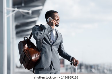 Business Talk. African Man Talking On Phone At Airport And Waiting Taxi