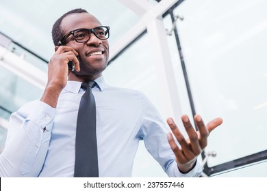 Business talk. Low angle view of confident young African man in shirt and tie talking on the mobile phone and gesturing