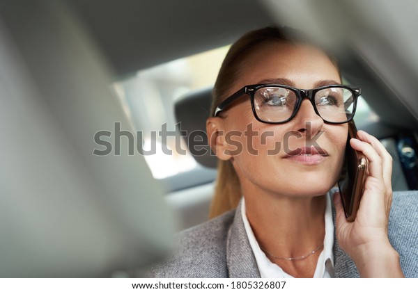 Business talk. Portrait of successful confident\
business woman wearing eyeglasses talking by mobile phone while\
sitting on back seat in the\
car