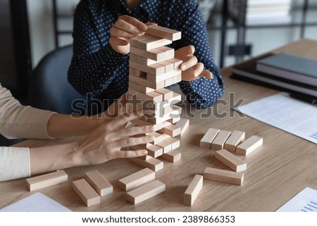 Business team colleagues playing jenga board game together, holding tower building, high stack of wooden blocks from falling, dealing with challenge, risk, teamwork and teambuilding skills. Close up