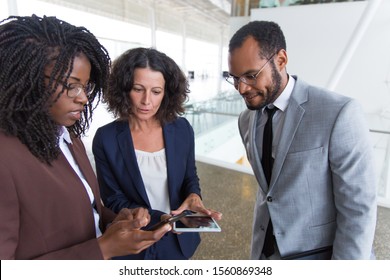 Business team consulting internet on digital devices together. Business man and women standing in modern office hallway, talking, using tablet and cellphone. Wireless communication concept - Shutterstock ID 1560869348