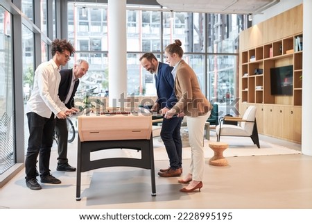 Business team have fun playing foosball competition at foosball table together in office