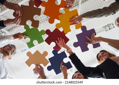 Business Team Holding Colorful Jigsaw Puzzle Parts. Group Of Different Multiracial People Suggest Creative Idea And Solution To Problem. Cropped Close Up Shot From Below. Teamwork, Innovation Concept