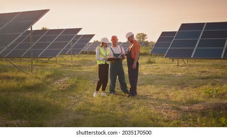 Business Team Of Industrial Technicians Walking Through Solar Park Outside. Construction Of Concentrated Solar Power Plant. Renewable Energy. Ecology. Technician And Investor Checking The Solar Panels