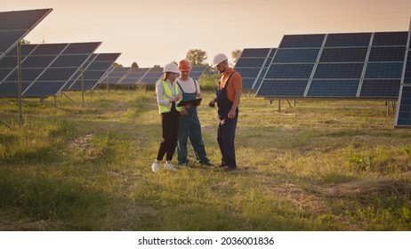 Business Team Of Industrial Technicians Walking Through Solar Park Outside. Construction Of Concentrated Solar Power Plant. Renewable Energy. Ecology. Technician And Investor Checking The Solar Panels