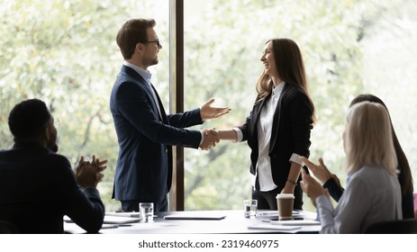 Business team leader congratulating employee on hiring, promotion, high work result, expressing recognition. Businessman shaking hands with female employee. Group applauding coworker success. - Powered by Shutterstock