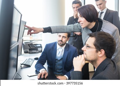 Business Team Looking At Data On Multiple Computer Screens In Corporate Office. Businesswoman Pointing On Screen. Business People Trading Online. Business, Entrepreneurship And Team Work Concept.