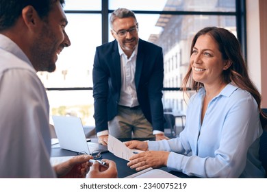 Business Team Meeting Around Office Boardroom Table With Laptops Discussing Documents - Powered by Shutterstock