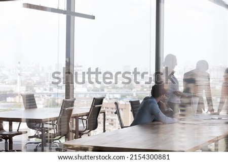 Business team meeting in contemporary business center, talking at office conference table, negotiating on project in modern interior with big panoramic window. Through glass view background