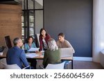 Business team meeting discussing  strategies around a conference table. Multiethnic businesswomen and mid adult businessmen in a serious team discussion during meeting. Colleagues collaborating.