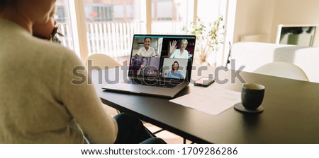 Business team meeting online over a video call on laptop. Woman sitting at table at home having a video conference with her colleagues.