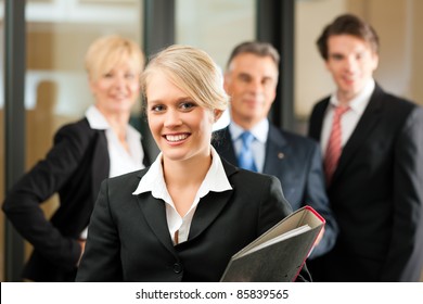 Business - Team In An Office; The Junior Manager Is Standing In Front