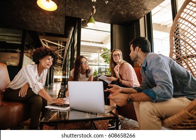 Business team sitting in office lobby and having a brainstorming session. Happy corporate business people sitting together with laptop and discussing. - Shutterstock ID 608658266