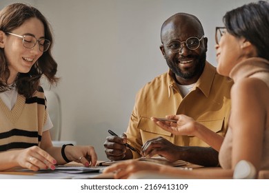Équipe d'affaires souriante et parlant les unes aux autres à table pendant la réunion au bureau : photo de stock